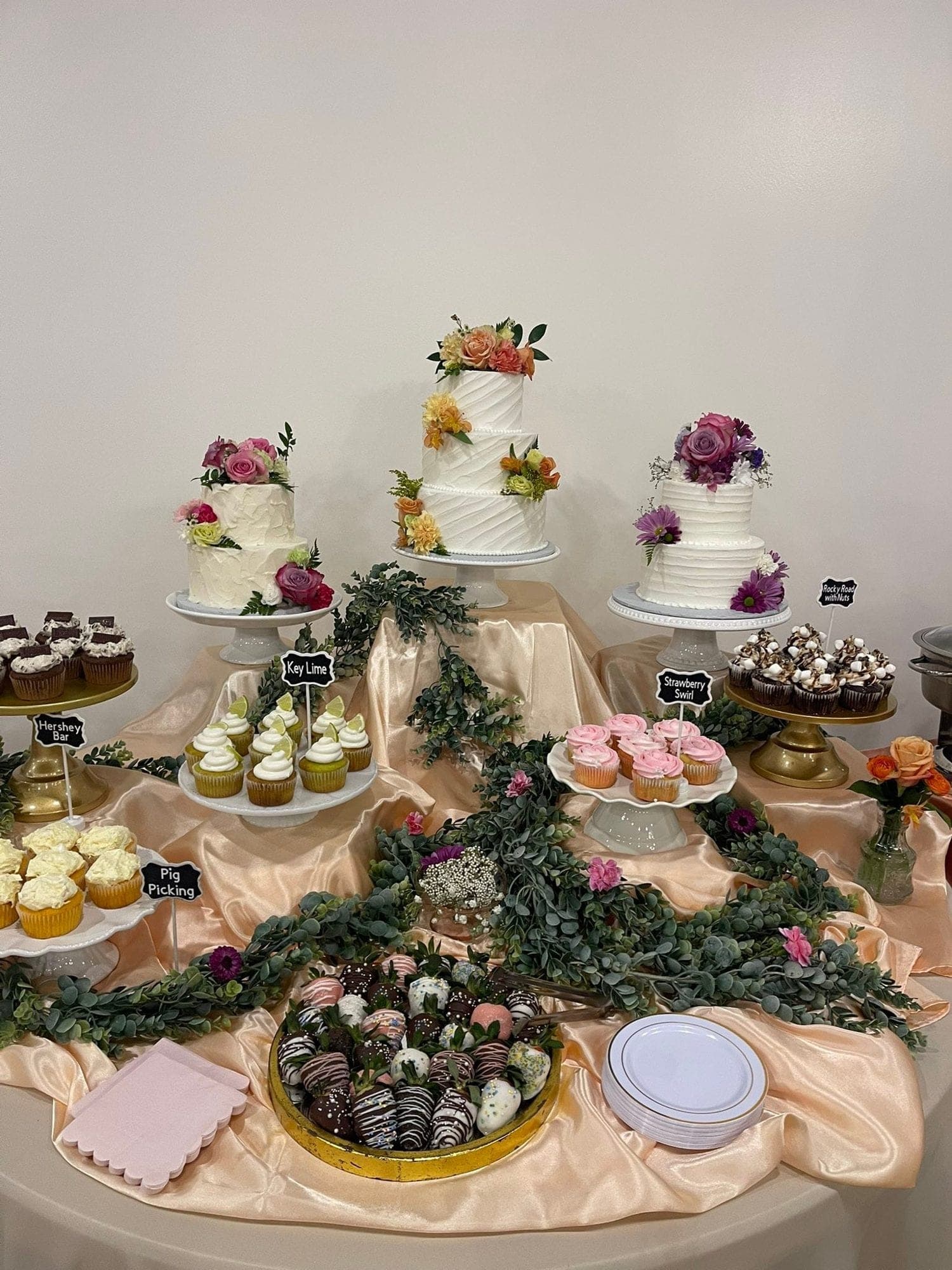 A table of wedding cakes, cupcakes, and chocolate-dipped strawberries